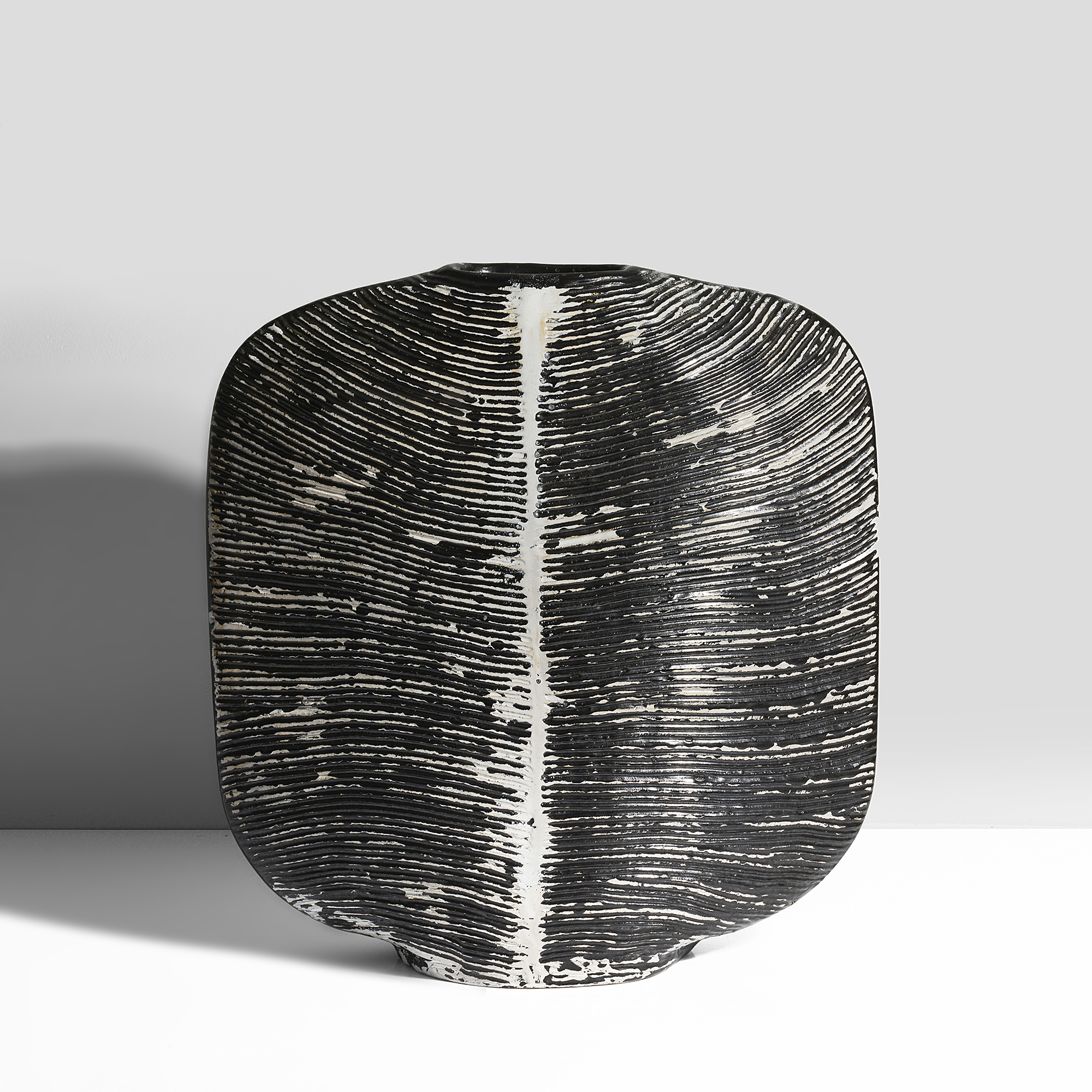 Earthenware, layered black and white tin glazes over a carved ribbed surface, incised signature and date