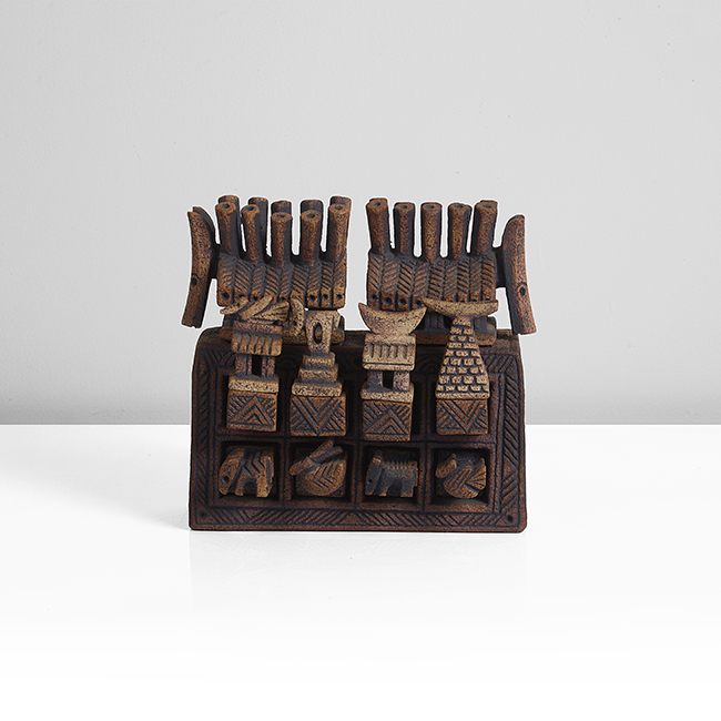 Stoneware Ceramic, dry brown glaze over intricately carved surface, the rectangular chest form set with eight small drawers, the top row of drawers with lids in the form of huts and towers mounted with a bird, beast, crescent moon and boat, the lower row set are carved with beasts made by Ian Godfrey