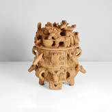 Stoneware ceramic, mottled brown and ochre glazes, the cylindrical vessel mounted with alternating carved fox heads and looping handles, the flat lid crowded with carved horses, horned beasts, rams and birds, raised on four carved feet by Ian Godfrey